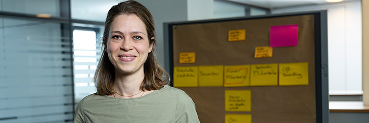 Eine Mitarbeiterin steht vor einer Pinnwand mit Notizzetteln in einem modernen Büro